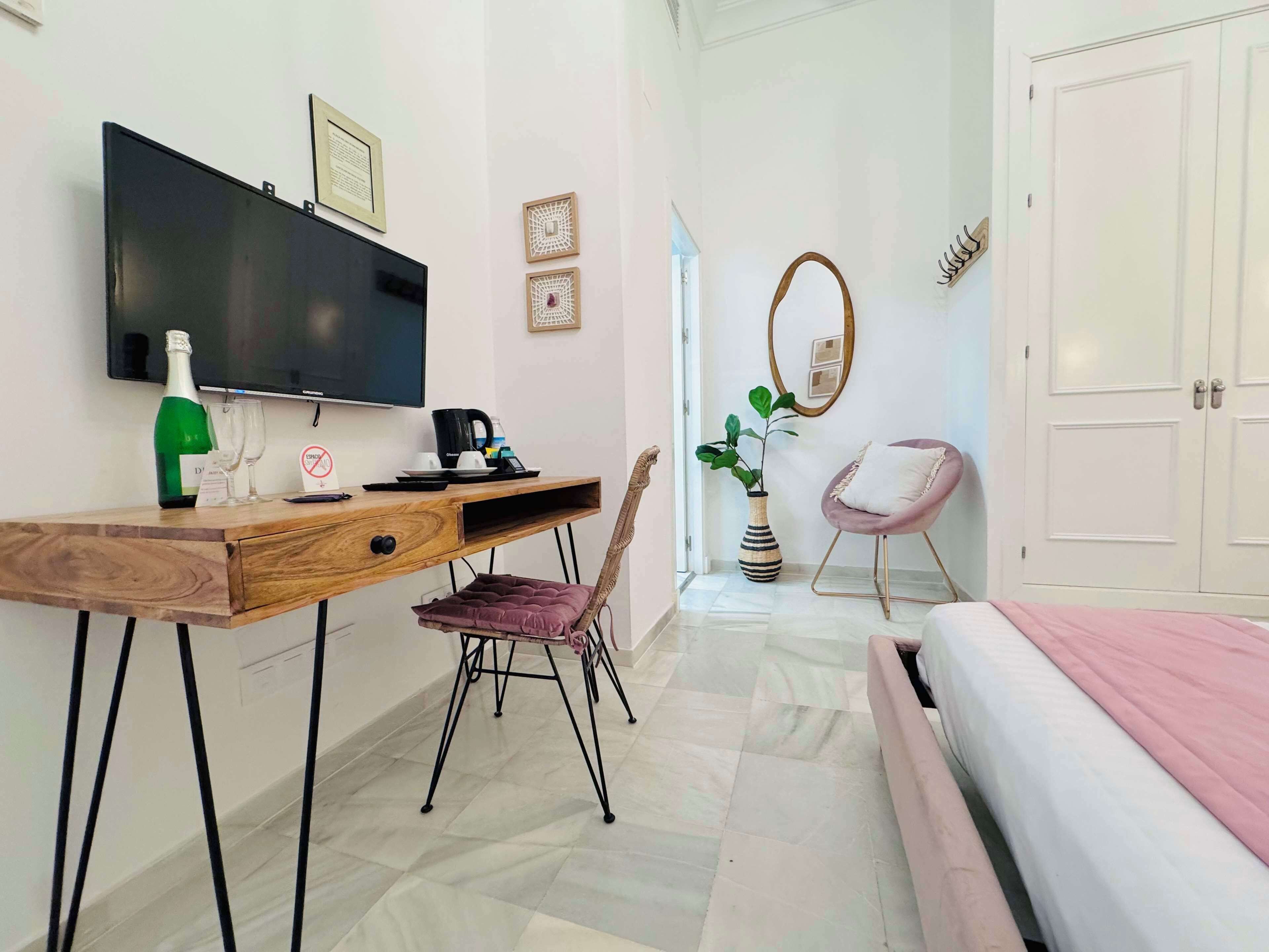 Una camera da letto moderna con un letto, una scrivania con un computer, una sedia, una TV e una porta che dà su un'altra stanza.
