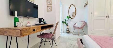 Una camera da letto moderna con un letto, una scrivania con un computer, una sedia, una TV e una porta che dà su un'altra stanza.