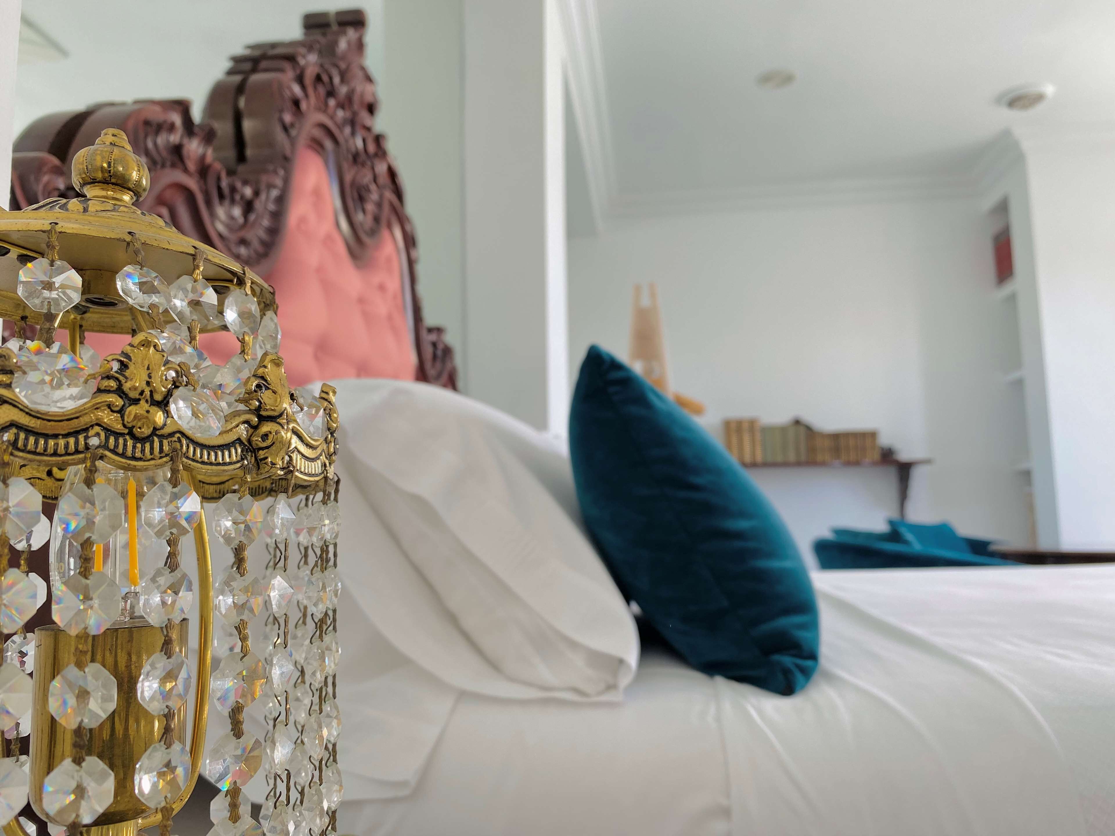 A bed with white and teal pillows, a gold ornate lamp with crystals, and a pink headboard.