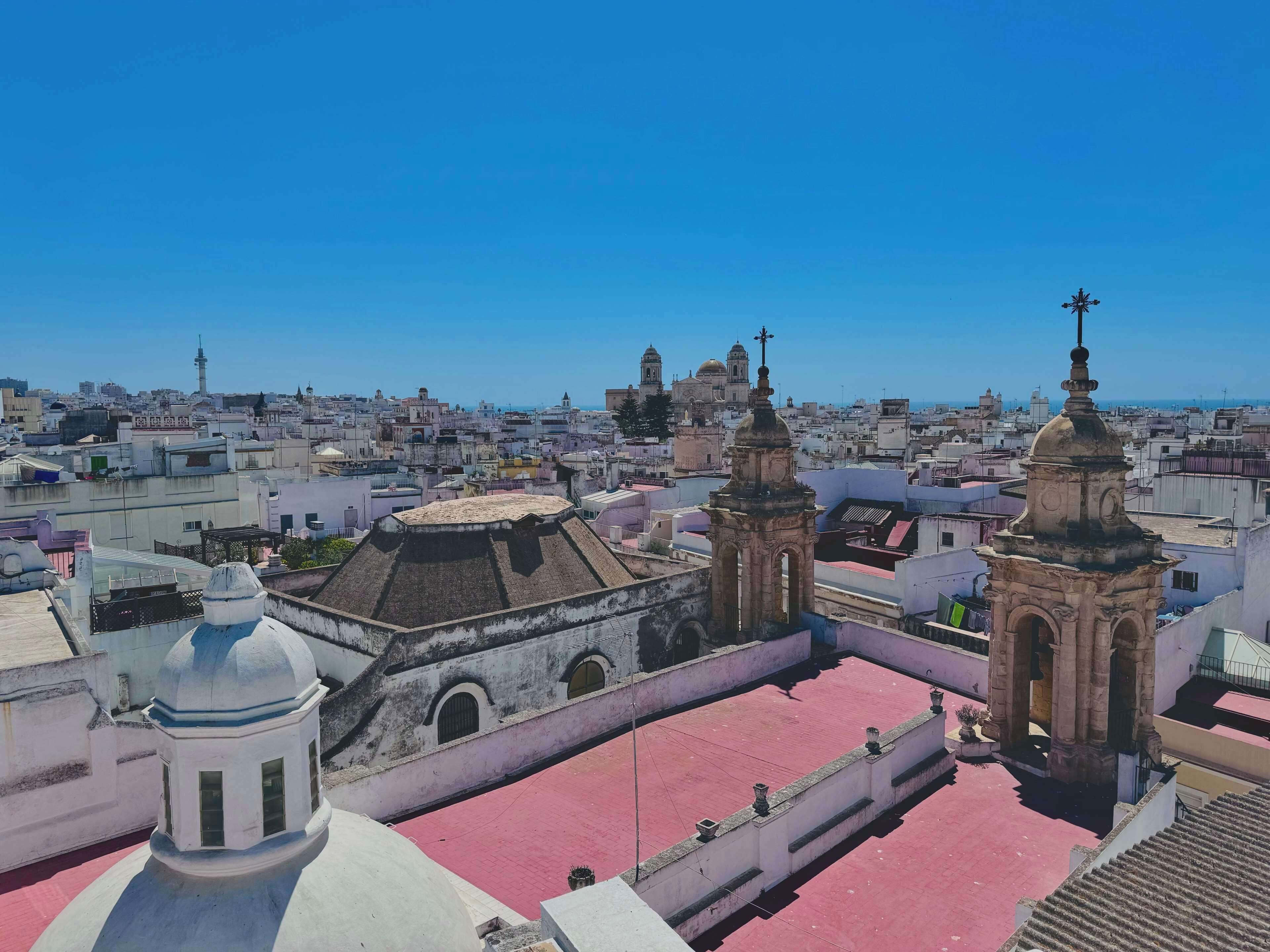 Un paisaje urbano con edificios históricos destacados, incluyendo una iglesia con tejado de tejas rojas y dos torres de campanas.