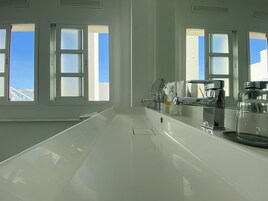 A modern kitchen with a large island, white countertops, and a view of the sky through the windows.