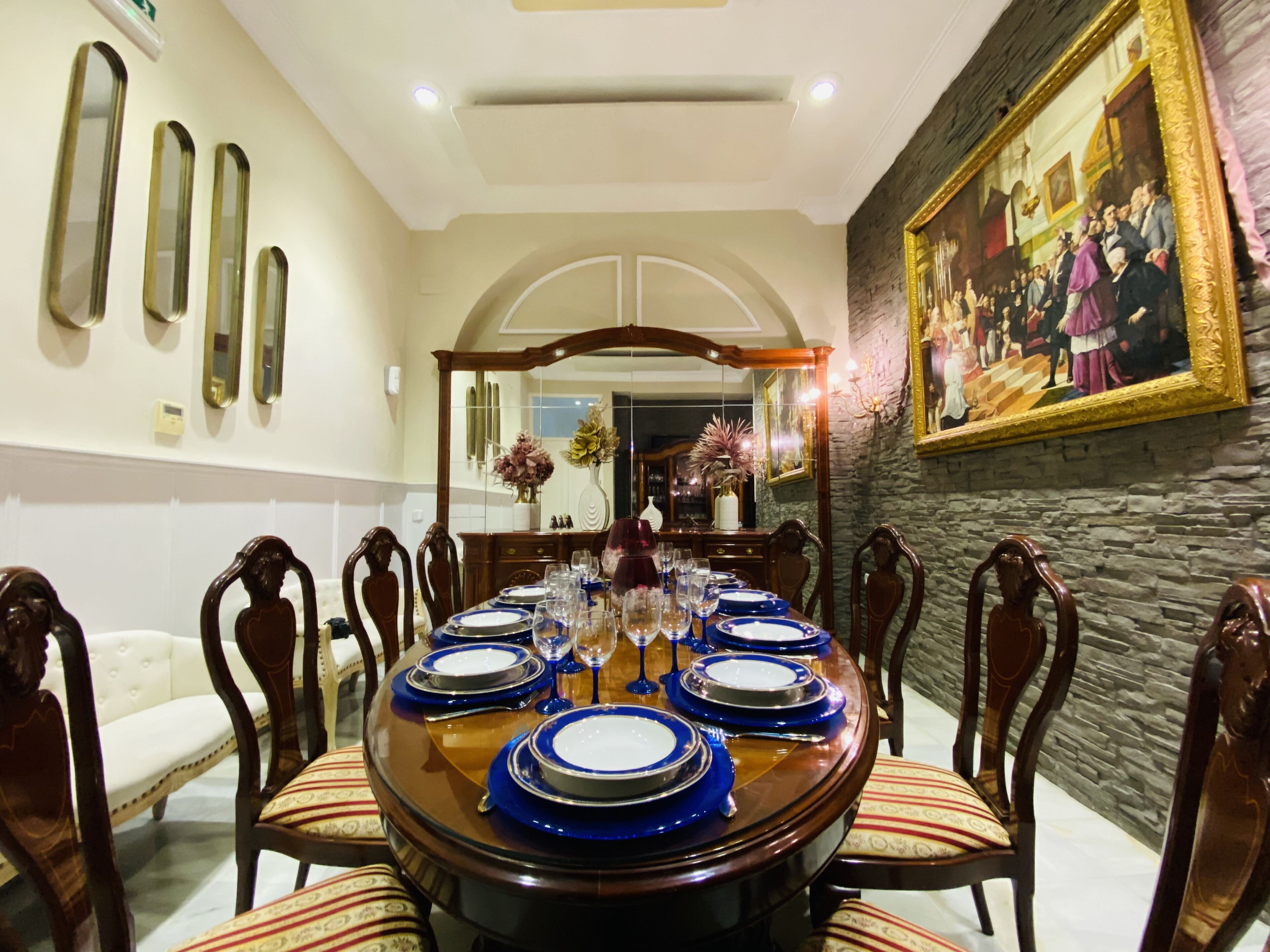 Uma sala de jantar formal com uma mesa redonda posta para seis pessoas, ladeada por cadeiras de madeira com assentos acolchoados.