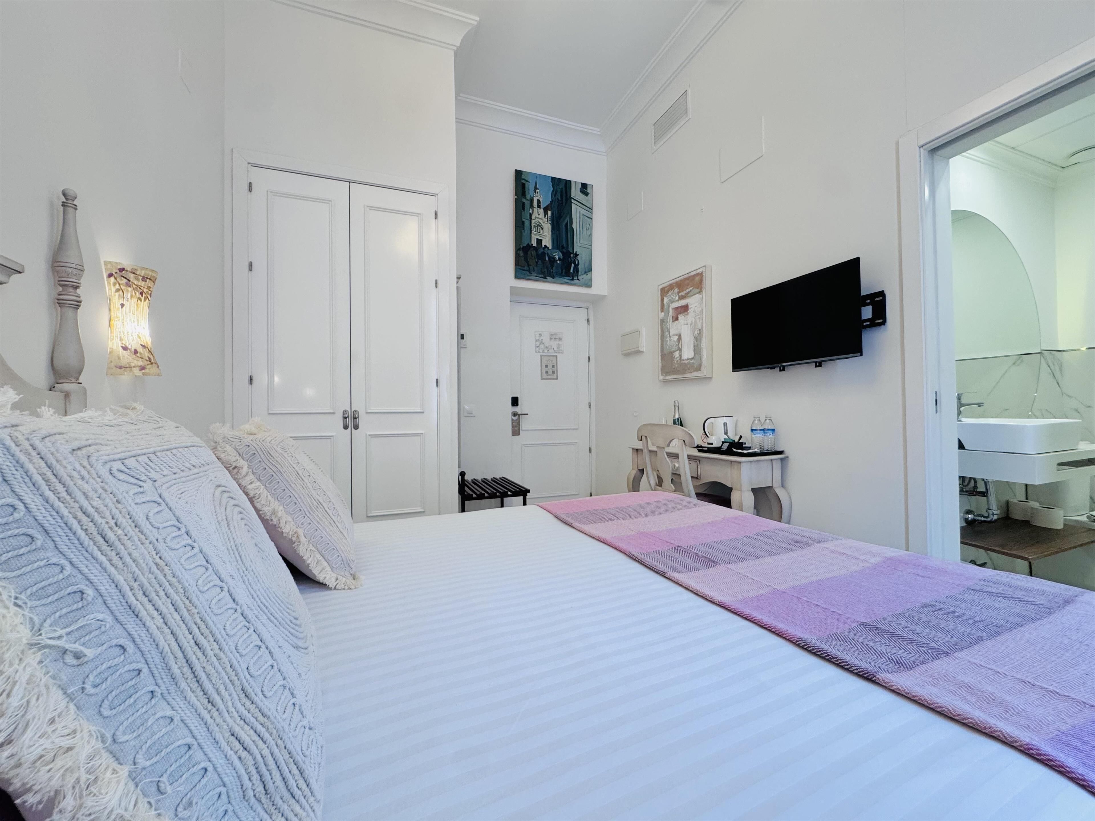 A bedroom with a large bed, a desk, a chair, a television, and a bathroom visible through an open door.