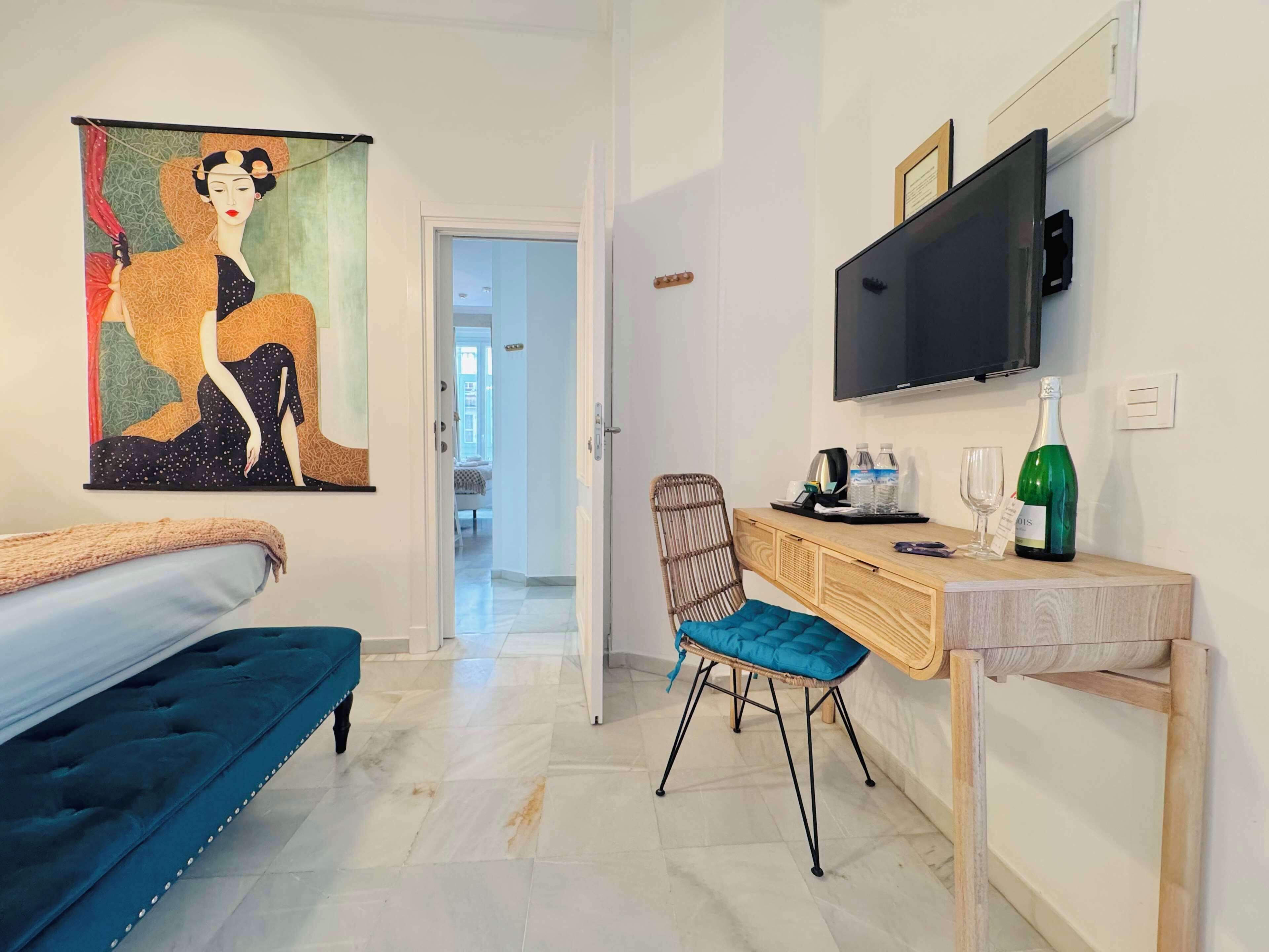 Quarto de hotel com cama, secretária com cadeira, televisão e um quadro na parede.