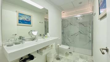 Un baño moderno con un tocador blanco, un espejo grande, una cabina de ducha de vidrio y piso de baldosas de mármol.