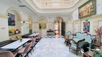 A spacious hotel lobby with a checkered floor, elegant seating, and a central staircase.