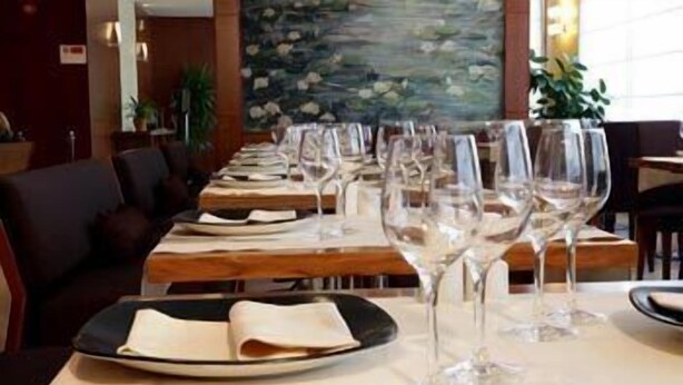 A restaurant with tables set for dining, featuring a painting on the wall and potted plants.