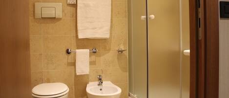 Un baño con inodoro, bidé y cabina de ducha de vidrio.