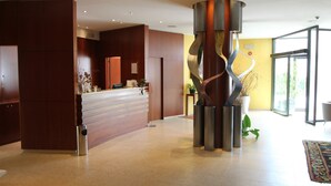 A reception area with a wooden reception desk, a modern sculpture, and a large glass door leading to a bright room.