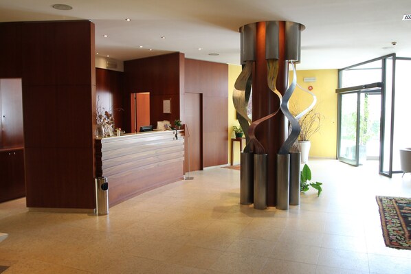A reception area with a wooden reception desk, a modern sculpture, and a large glass door leading to a bright room.