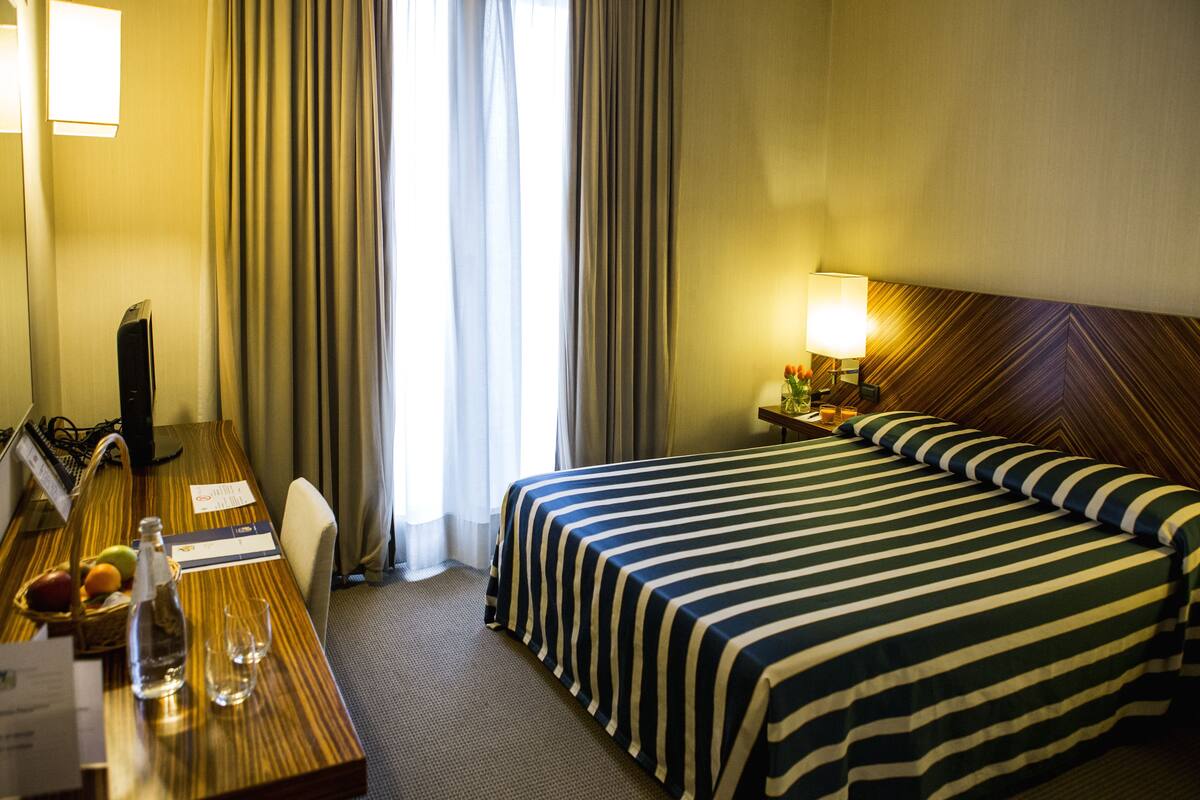 Une chambre d’hôtel avec un grand lit, un bureau avec un ordinateur, une lampe et une fenêtre avec des rideaux.
