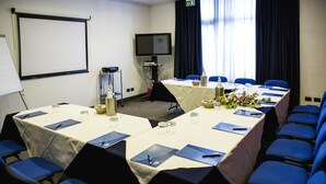 A conference room with a long table, blue chairs, a projector screen, and a television.
