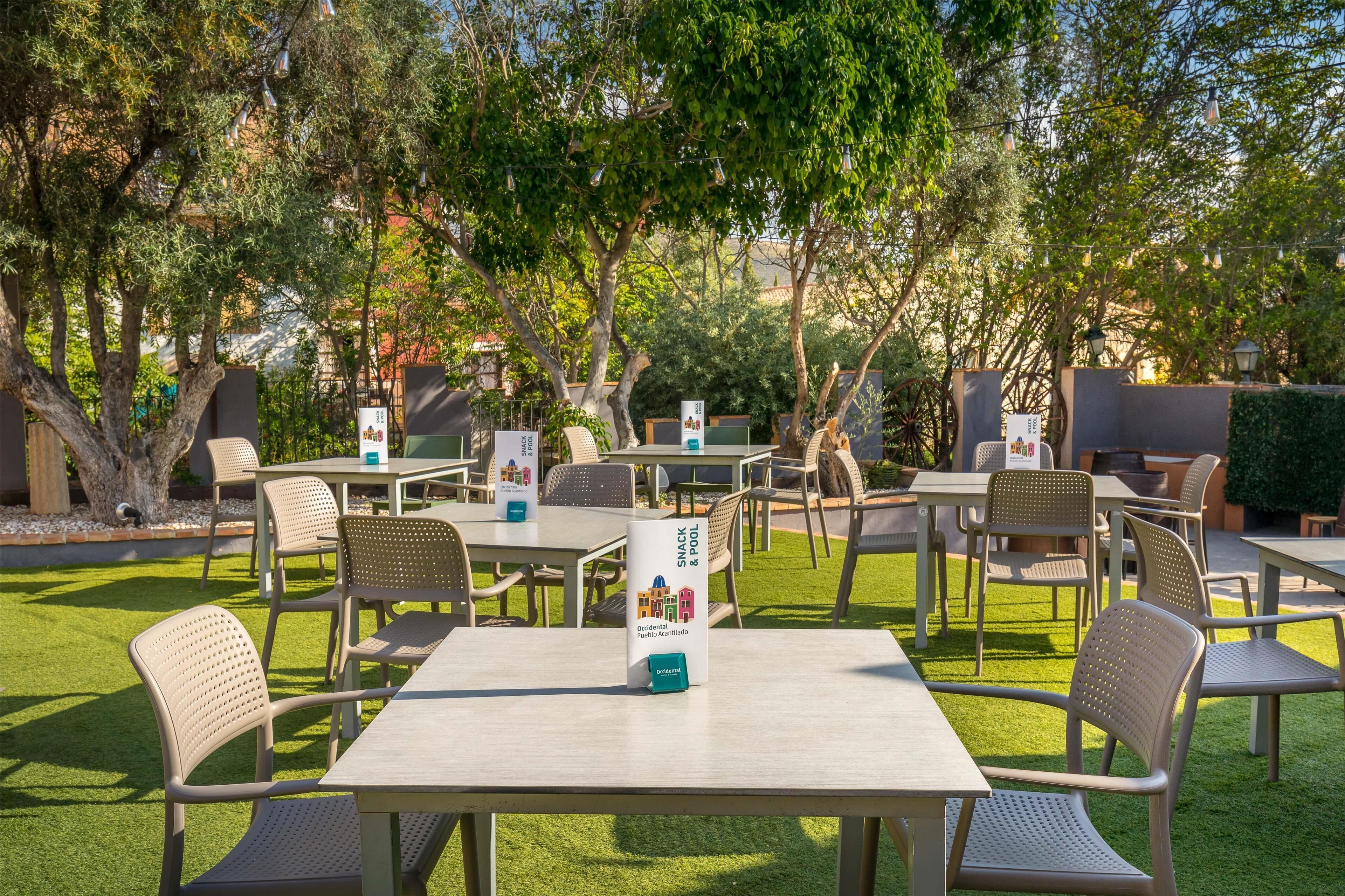 An outdoor seating area with tables and chairs, surrounded by trees and greenery.
