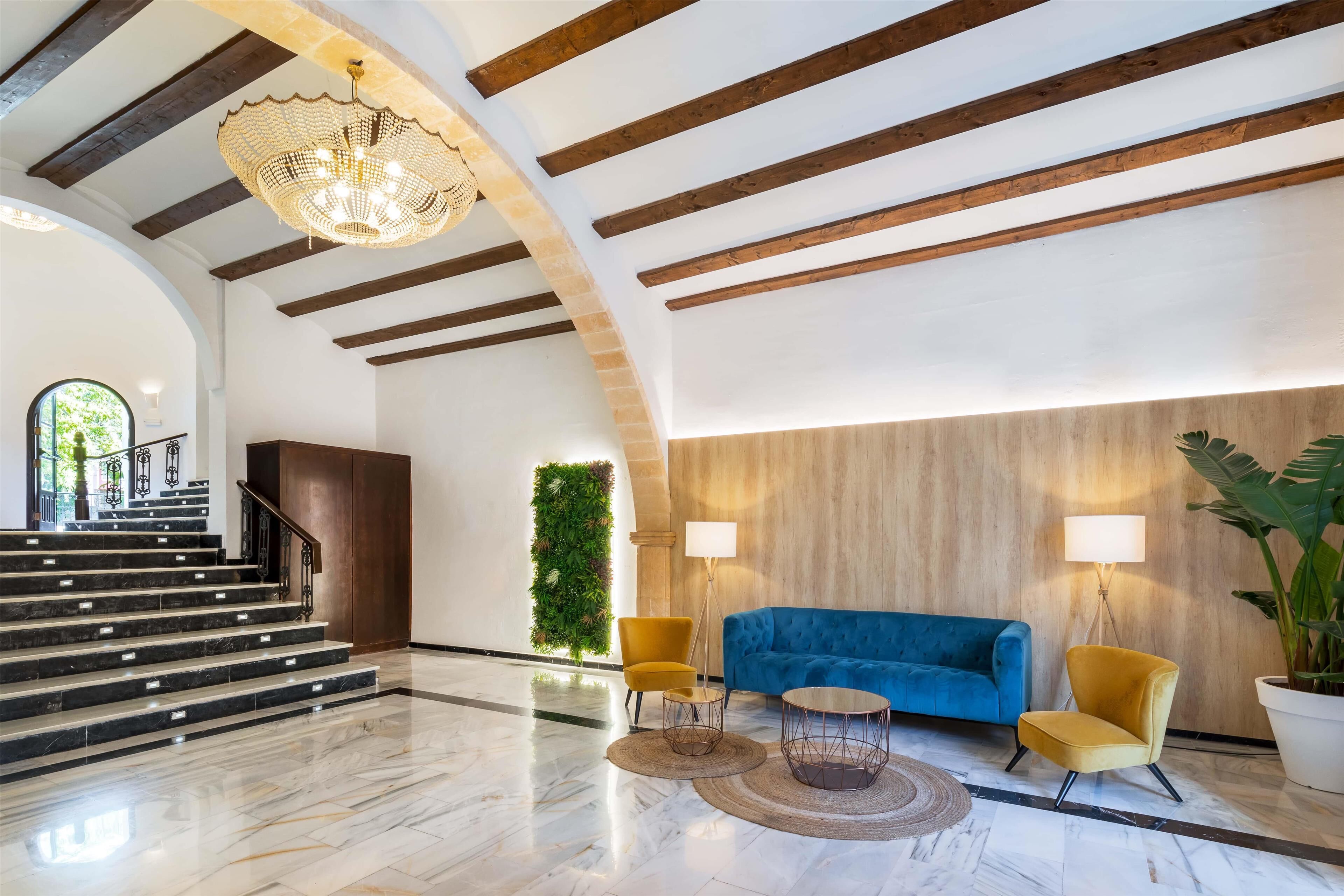 A spacious lobby with a marble floor, a staircase, a blue sofa, yellow chairs, and a large potted plant.