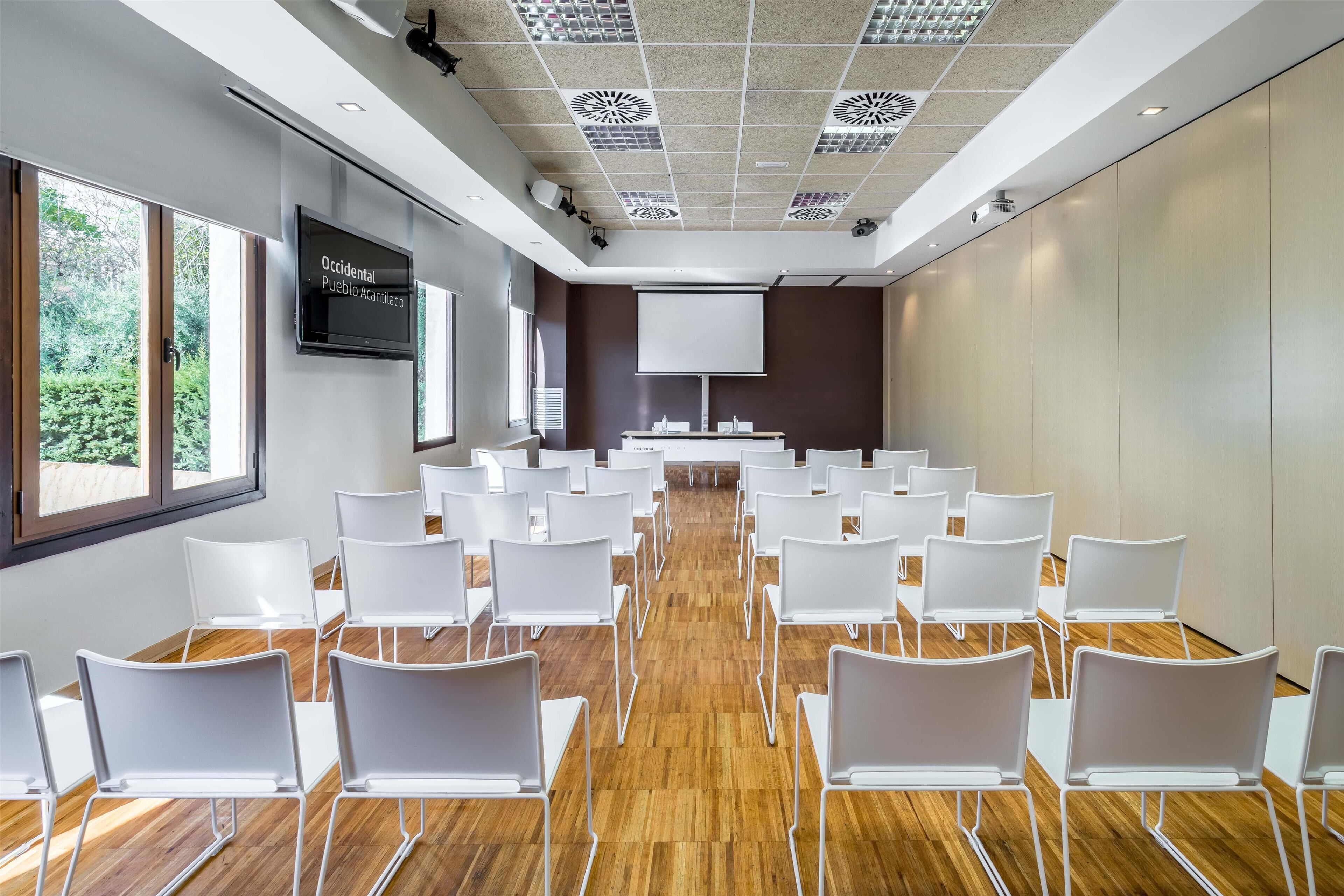 A conference room with white chairs arranged in rows, a large screen, and a projector.