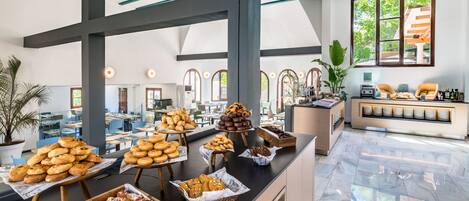 A buffet area with various food items displayed on wooden stands and baskets, a seating area with chairs and a sofa, and large windows allowing natural light.