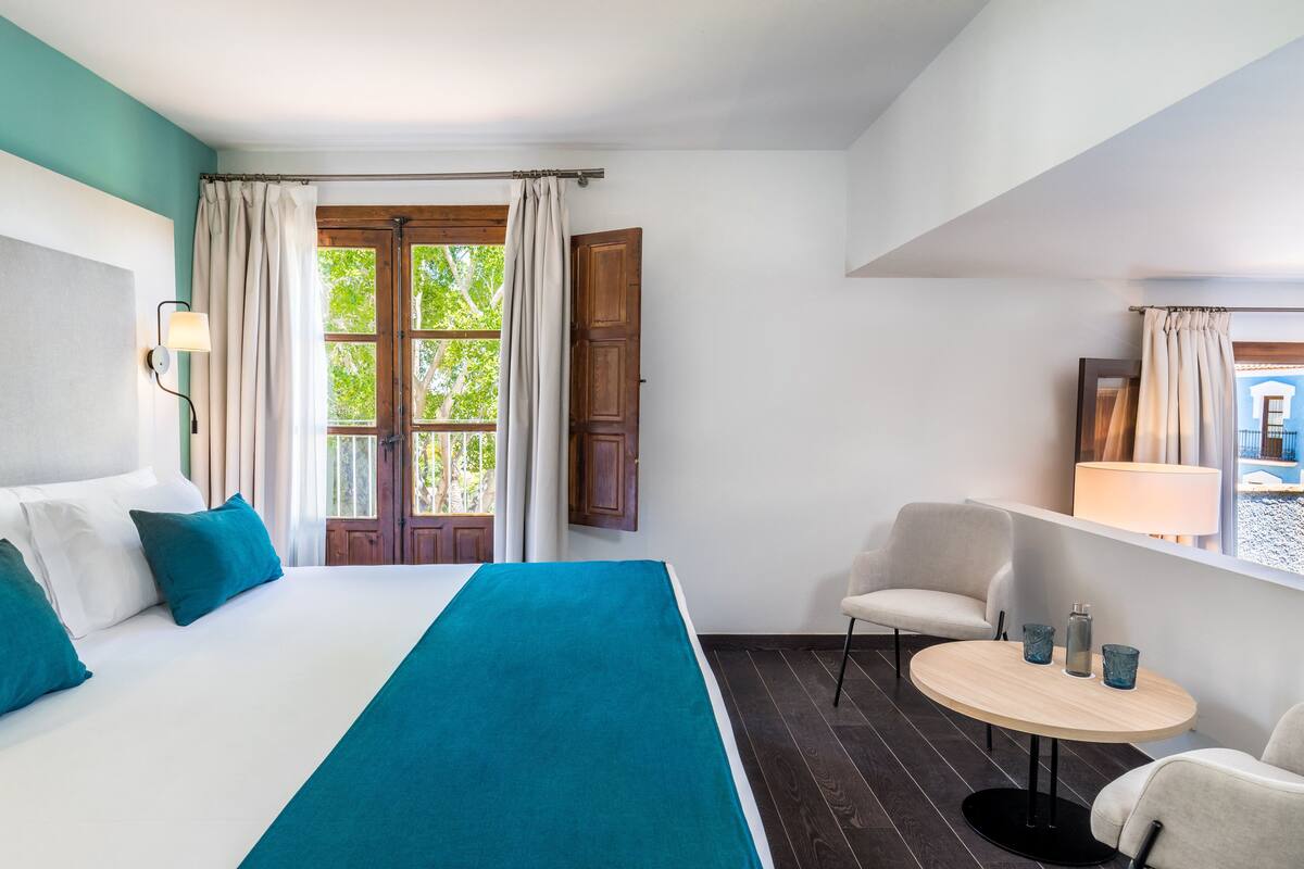 Une chambre d’hôtel avec un lit, une petite table ronde avec deux tasses, une chaise et une fenêtre avec des rideaux.