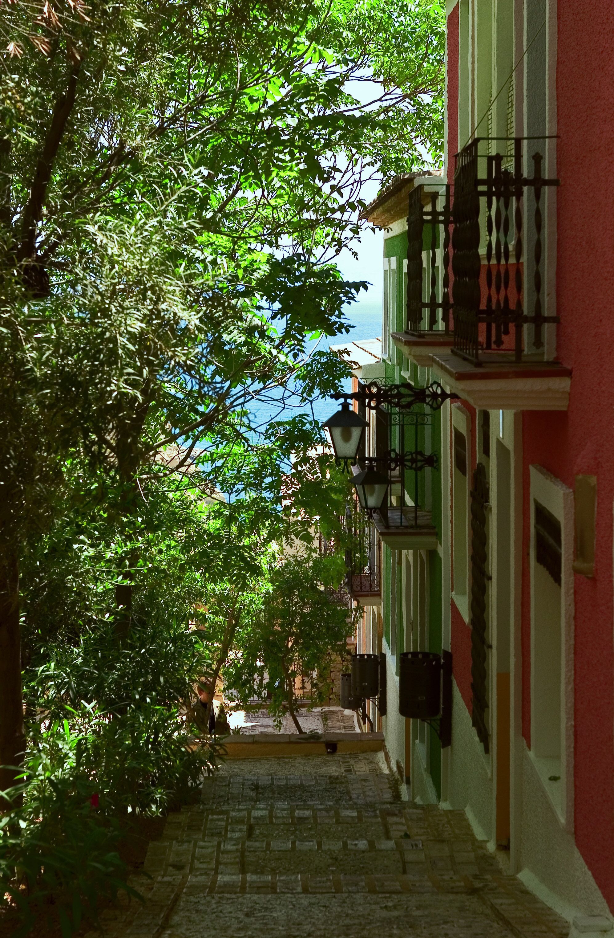 A narrow cobblestone street flanked by buildings with balconies and hanging lanterns.
