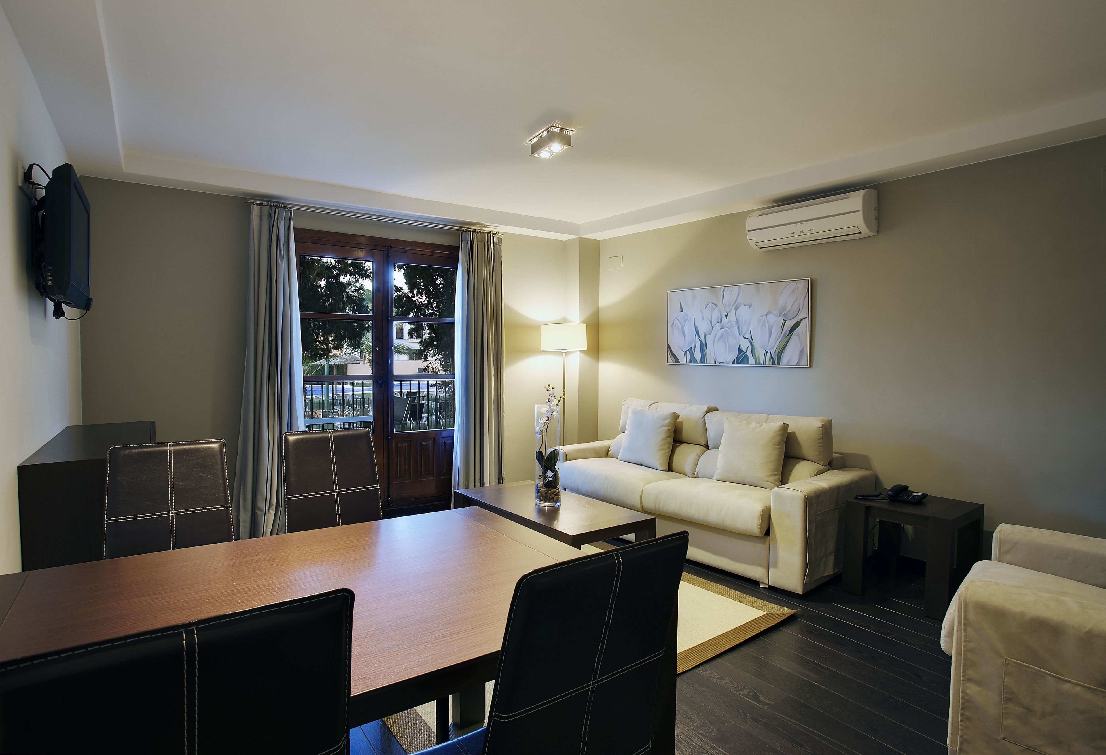 A modern hotel room with a dining area, a sofa, a lamp, and an air conditioning unit.