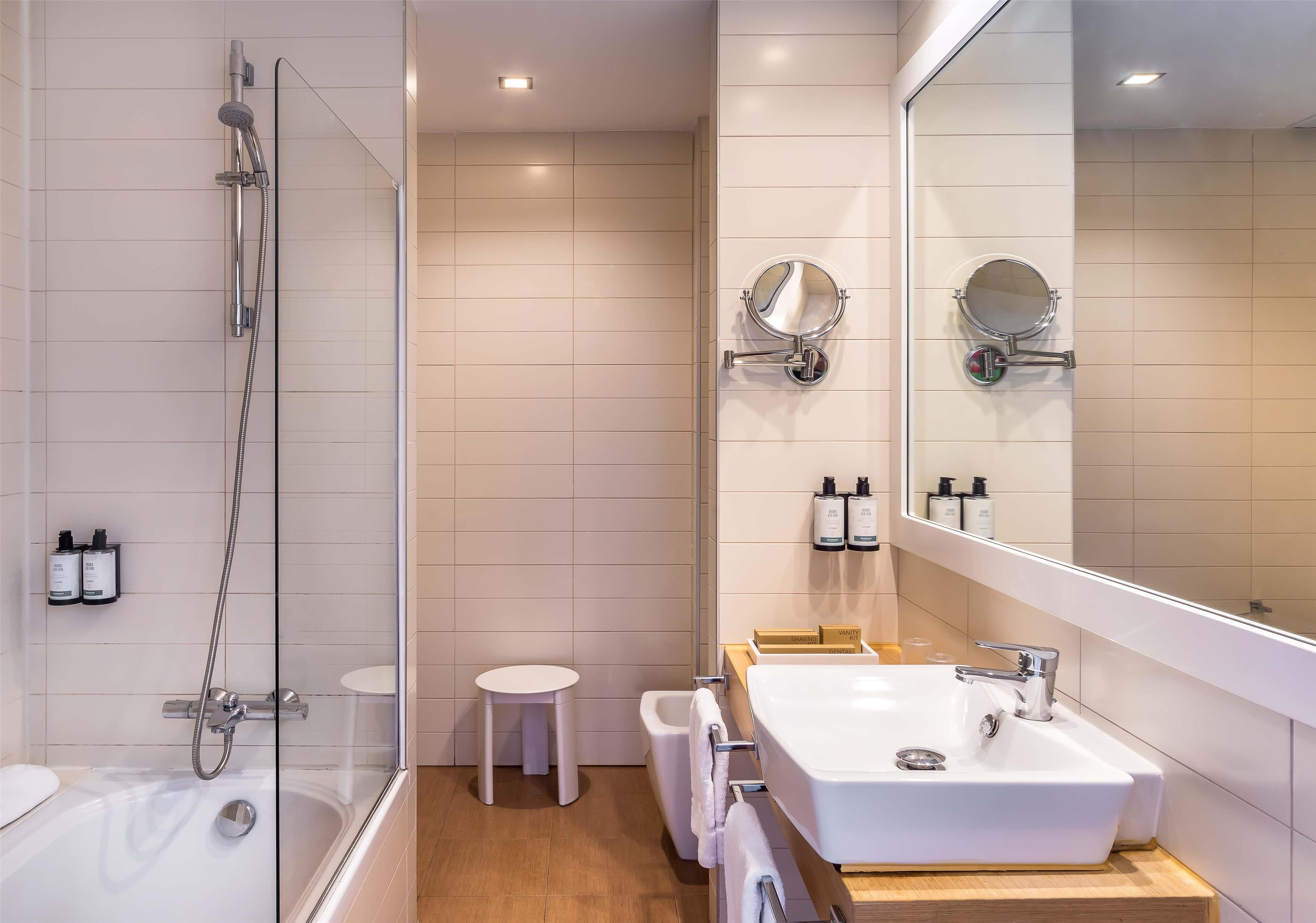 A modern bathroom with a glass-enclosed shower, a white sink with a wooden countertop, and a large mirror.