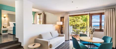 A modern hotel room with a sofa, a small table, and a balcony with a view of the sea.