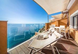 Un balcón con vista al mar, una mesa y sillas.