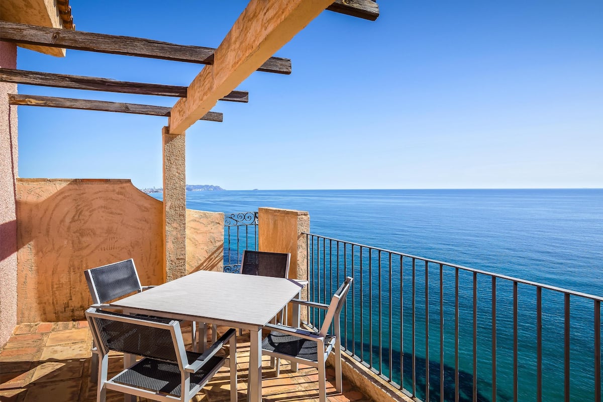 Une terrasse avec une table et des chaises, donnant sur une mer d’un bleu limpide.