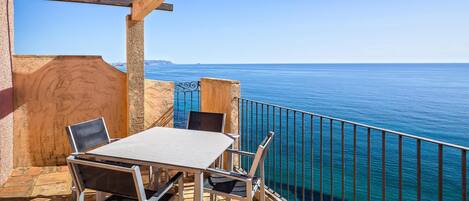 A terrace with a table and chairs, overlooking a clear blue sea.