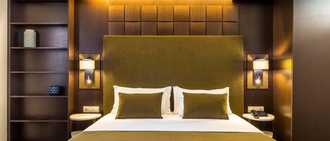 A modern hotel room with a large bed, two bedside tables, a small round table, and built-in shelving.