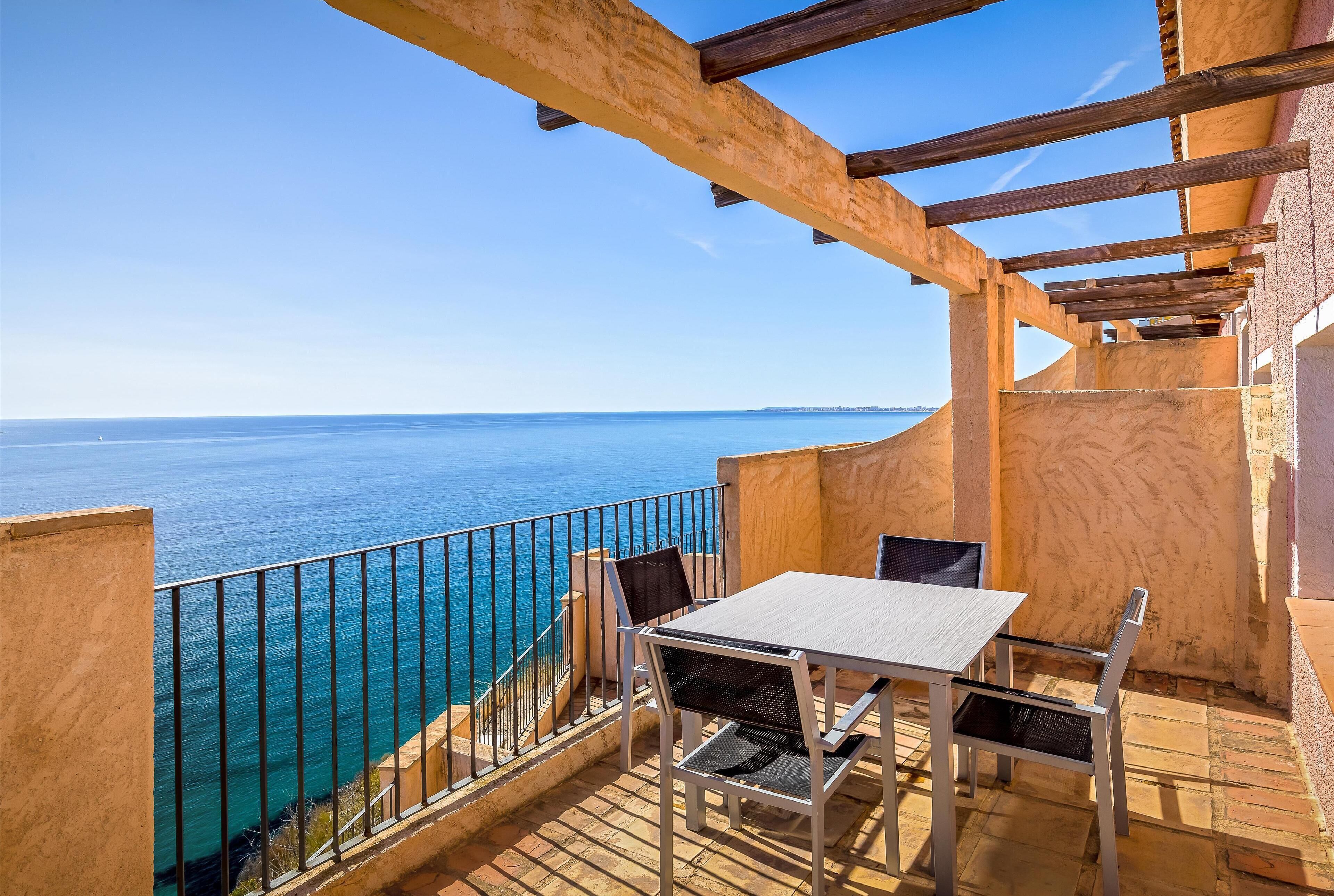 A balcony with a table and chairs overlooking the sea.