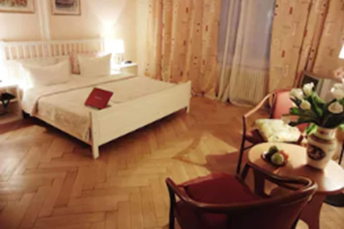 Ein Hotelzimmer mit Bett, Nachttisch, Stuhl und einem Tisch mit Blumenvase.