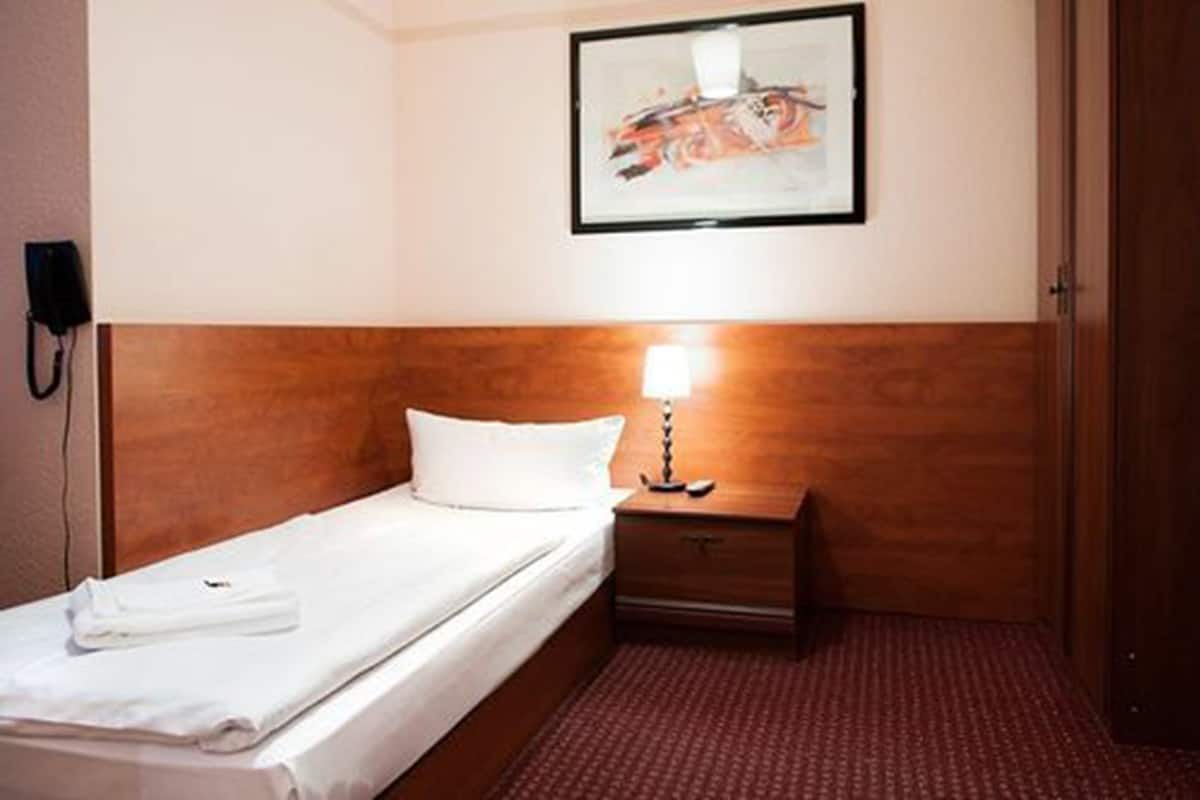Ein Hotelzimmer mit einem Einzelbett, einem Nachttisch mit Lampe, einem gerahmten abstrakten Gemälde an der Wand und einem Telefon.