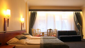 A hotel room with a bed, a sofa, a table with chairs, and a window with curtains. - Kurfürst am Kurfürstendamm (Berlin)