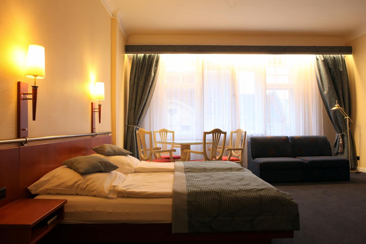 Ein Hotelzimmer mit Bett, einer Couch, einem Tisch mit Stühlen und einem Fenster mit Vorhängen.