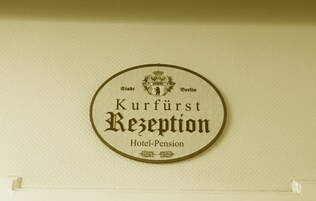 A circular sign with the text "Kurfürst Rezeption Hotel-Pension" on a textured wall.