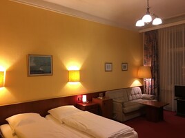 A hotel room with two beds, a sofa, a TV, and a lamp.