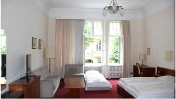 Habitación de hotel con cama, escritorio, silla, televisor y ventana con cortinas.