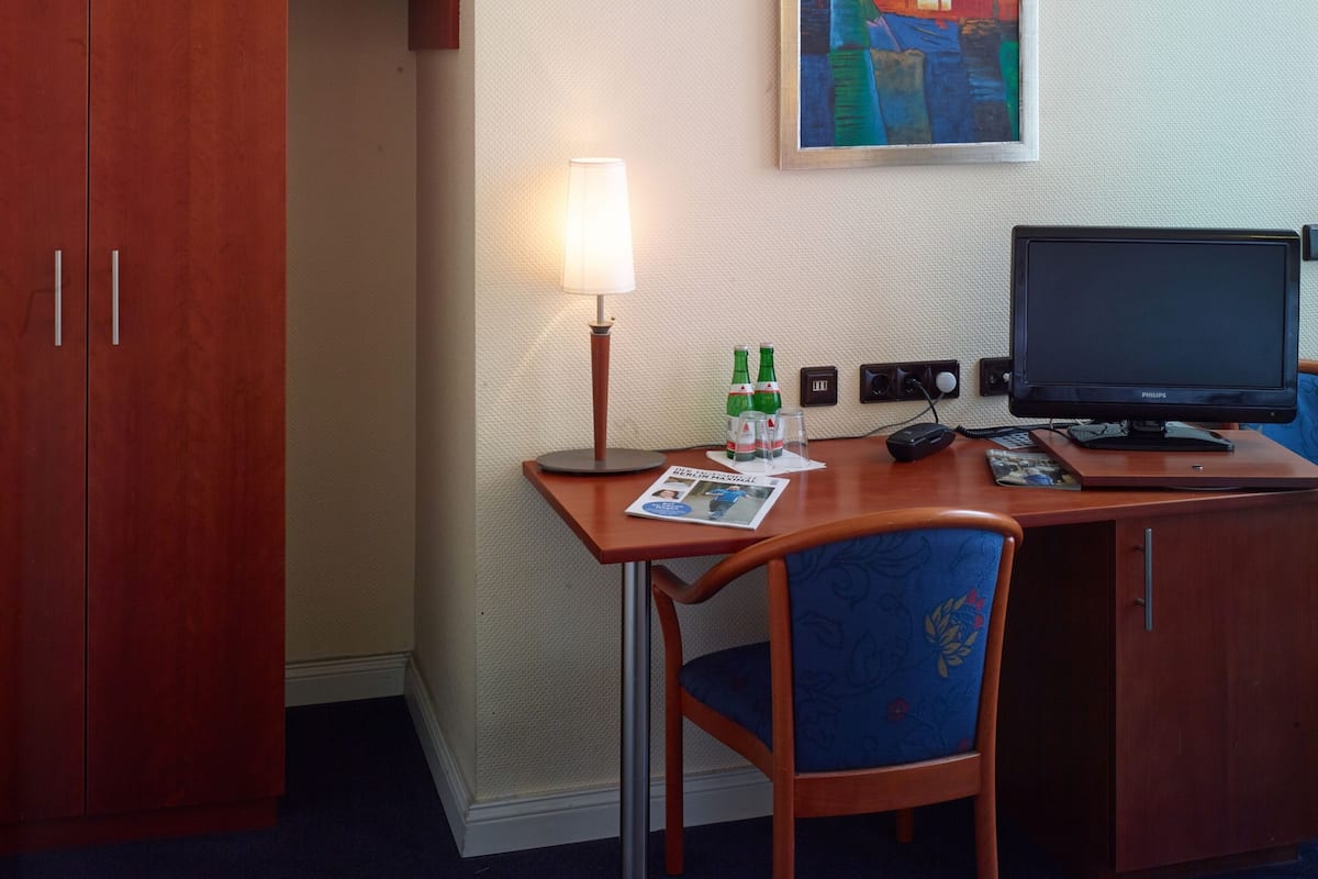 Ein Hotelzimmer mit Holzschreibtisch, einem Sessel, einem Fernseher, einer Lampe und einem Bild an der Wand.