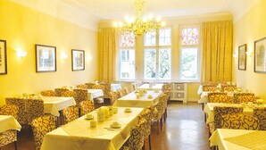 A dining area with multiple tables and chairs, large windows with curtains, and a chandelier. - Kurfürst am Kurfürstendamm (Berlin)