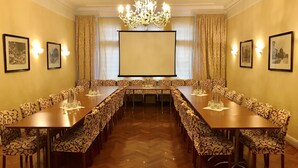 A conference room with a long table, patterned chairs, a chandelier, and framed pictures on the walls. - Kurfürst am Kurfürstendamm (Berlin)