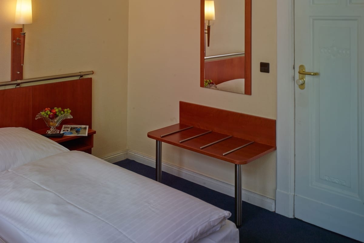 Ein Hotelzimmer mit einem Bett, einem Nachttisch mit Lampe und Obstschale, einem Spiegel und einer Tür.
