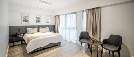 Una habitación de hotel moderna con una cama grande, dos sillones, una mesita y un escritorio con lámpara.