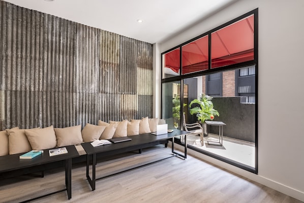Una sala de estar moderna con un sofá negro, una mesa de centro y un gran ventanal con una persiana roja.