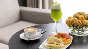 A table with a cup of coffee, a glass of green beverage, and a plate of fruit and nuts.