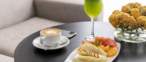 Una mesa con una taza de café, un vaso de bebida verde y un plato de fruta y frutos secos.