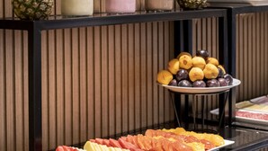 A buffet with various fruits, beverages, and stacked plates.