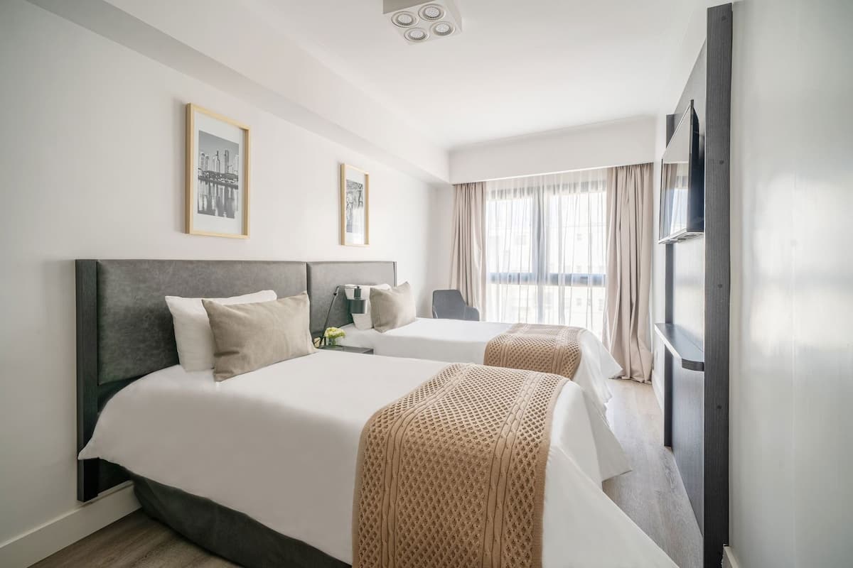 A hotel room with two beds, a TV, and a window with curtains.