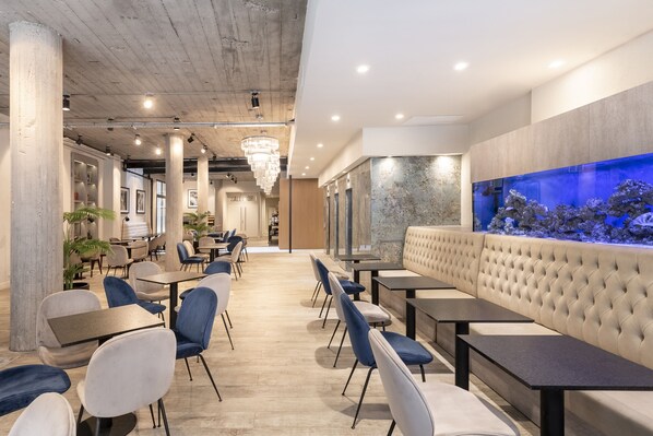 A modern restaurant interior with a long counter, blue and white chairs, a large aquarium, and a chandelier. - Efe Hotel & Cowork (Buenos Aires)