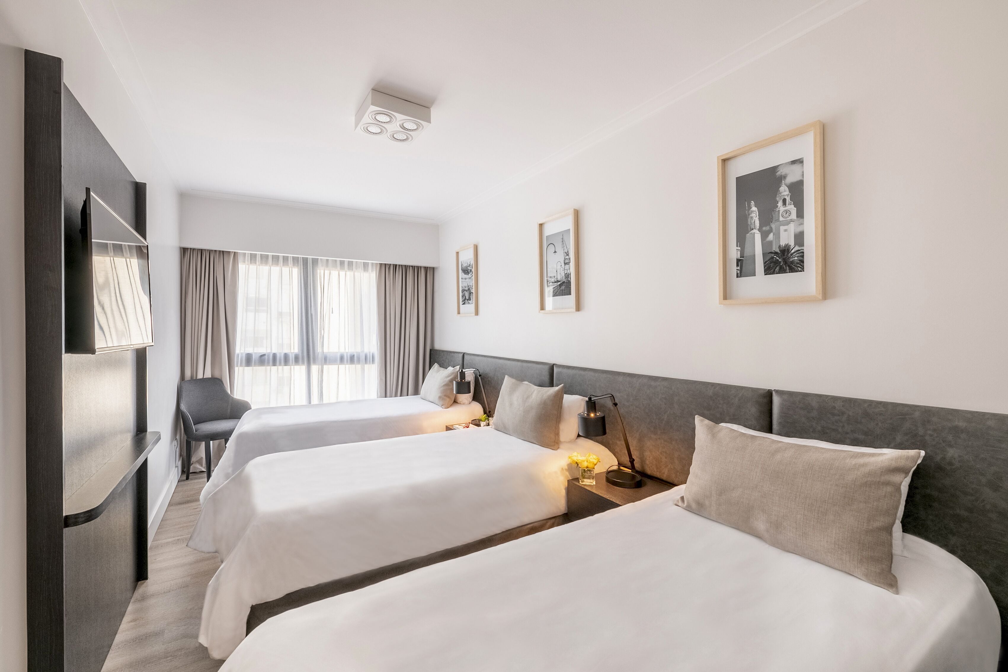 Una habitación de hotel con dos camas, un escritorio, una silla y un ventanal con cortinas.