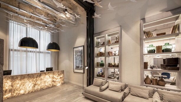 A modern living room with a wooden reception desk, a beige sofa, and shelves with decorative items.